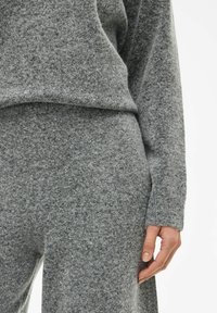 Szary sweter dzianinowy i pasujące spodnie, wykonane z miękkiego materiału o teksturowanej powierzchni. Luźny krój z okrągłym dekoltem i długimi rękawami.