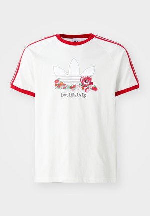 Biała koszulka z czerwonym kołnierzem i lamówką na rękawach, z kwiatowym logo Adidas i uśmiechniętym sercem w stylu kreskówki z napisem „Love Lifts Us Up”.