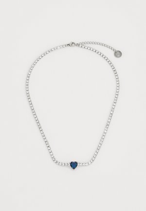 Collier en strass avec une chaîne en argent, présentant une gemme bleue en forme de cœur au centre, des pierres transparentes brillantes alternées et un petit fermoir.