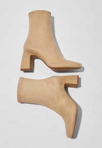 Stivali alla caviglia beige in materiale simile alla pelle scamosciata. Presentano un tacco a blocco, punta affusolata e un design senza cuciture con dettagli di cucitura visibili.
