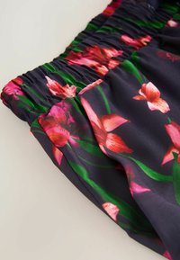 Bloemmotief stof met levendige roze bloemen en groene bladeren op een donkere achtergrond, met een elastische tailleband en een zachte textuur.