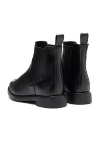 Melnu ādas Chelsea zābaku pāris ar elastīgām sānu pannām un vilkšanas cilpām, attēlots no aizmugures uz baltas fona.