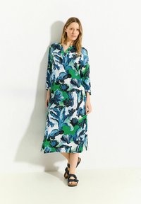Langes, locker sitzendes Kleid aus leichtem Stoff. Mit einem lebhaften blauen, grünen und schwarzen Blumenmuster. Mit eingeschnittenem Kragen und dreiviertel Ärmeln.