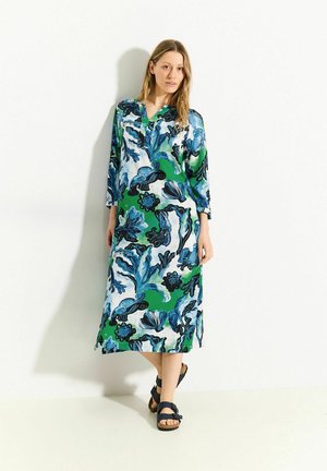 Lange, losvallende jurk van lichtgewicht stof. Heeft een levendig blauw, groen en zwart bloemenpatroon. Met een notch-kraag en driekwart mouwen.