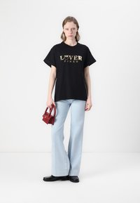 Juoda trumpomis rankovėmis marškinėliai su auksinėmis užrašais "LOVER" ir "PINKO", derinami su šviesiai mėlynomis platėjančiomis džinsomis ir mažais raudonais rankinukais.