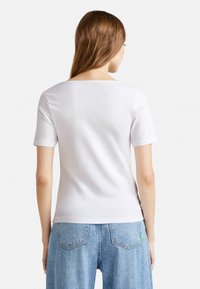 Bílý krátký rukáv s jednoduchým kulatým výstřihem, hladkou texturou a přiléhavým střihem, v kombinaci se světle modrými širokými džíny.