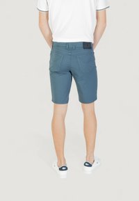 Pantalones cortos de algodón azules con un diseño ajustado, que cuentan con bolsillos traseros y una etiqueta negra en la cinturilla. Llevados con zapatillas blancas.