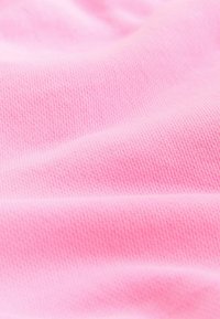 Mehka roza tkanina z drobno pleteno teksturo in nežnimi gubami, ki ustvarjajo subtilne sence in poudarke.