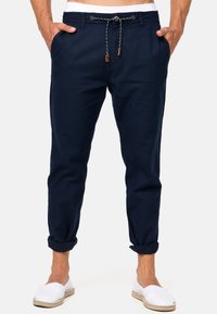 Pantaloni in lino blu navy con vita regolabile tramite cordino, orli arrotolati e tasche laterali. Presentano un cordino intrecciato con un accento in pelle.