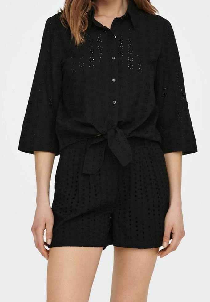 Camicia nera a maniche corte con bottoni e nodo davanti, caratterizzata da un motivo occhiello e tessuto testurizzato. Abbinata a pantaloni corti neri coordinati.