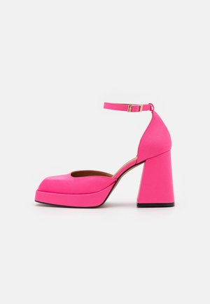 Talons compensés rose vif avec talon bloc épais et bride de cheville avec boucle dorée sur fond blanc.
