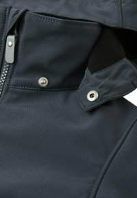 Gros plan sur une veste imperméable sombre, dotée d'une fermeture éclair et de boutons-pression, avec un intérieur en polaire douce visible près du col.
