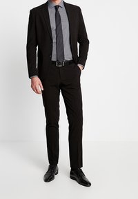 Černý blazer, šedá košile s puntíky, tmavá kravata, černý opasek, slim-fit černé kalhoty, lesklé černé boty, minimalistický design.