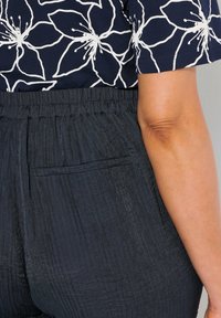 Marinblus med vitt blommönster i kombination med mörka, strukturerade byxor som har elastiskt midjeband och en bakficka.