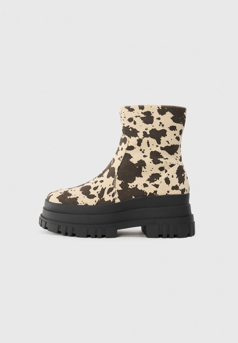 Bocanci grosolon în beige și imprimeu de vacă negru, având o talpă din cauciuc groasă și un superior din țesătură texturată. Siluetă elegantă și modernă.