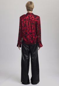 Rode transparante blouse met zwart bloemenpatroon, lange mouwen en knopen. Gecombineerd met zwarte wijde broeken van nepleer.