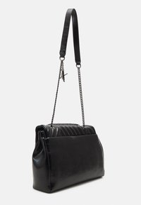Borsa in pelle nera con frontale trapuntato, base piatta e tracolla con dettagli in catena. Texture liscia con una silhouette strutturata.