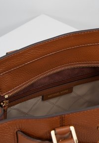 Wnętrze brązowej skórzanej torebki z zamkiem błyskawicznym, z miękkim zamszowym wykończeniem i metką z napisem "MICHAEL KORS". Złote akcenty.
