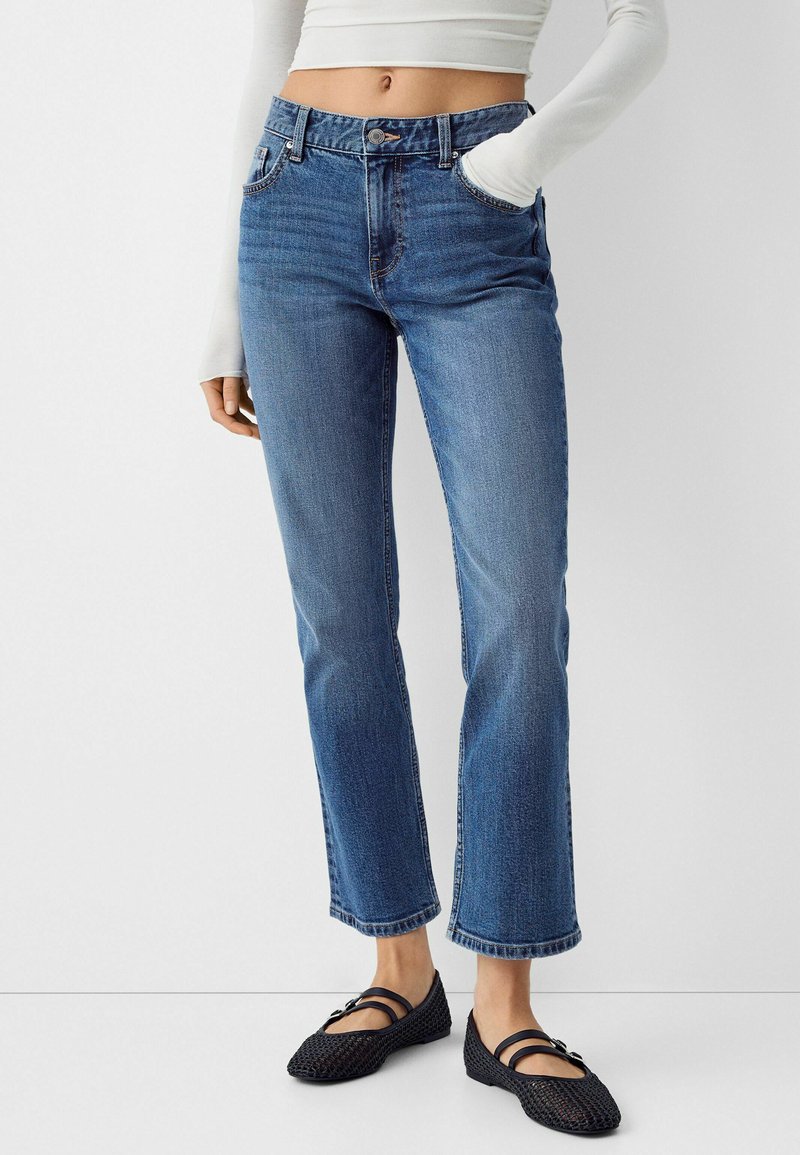 Jeans in denim blu con vita aderente, gamba dritta e leggero sfilacciamento agli orli. Abbinati a ballerine nere con texture.