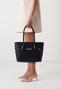 Zwarte leren tote bag met dubbele handvatten, gouden hardware en een gladde textuur. De tas heeft een eenvoudig, gestructureerd ontwerp.