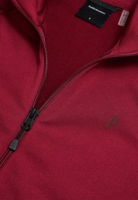 Rød polyester zip-jakke med en glat tekstur, kontrastfarvet sort lynlås og et lille, mørkt logo på brystet.