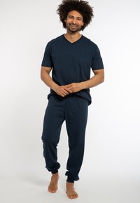 Set di pigiama in cotone blu navy composto da una maglietta a maniche corte con scollatura a V e tasca, abbinata a pantaloni con polsini elastici e vestibilità rilassata.
