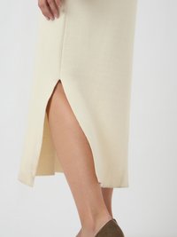 Donna che indossa una gonna midi crema con uno spacco frontale, che mostra parte della sua gamba, abbinata a scarpe a punta in suede marrone.