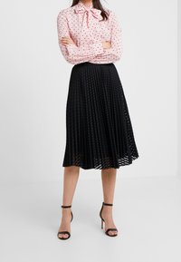 Blusa rosa a pois con colletto a fiocco, abbinata a una gonna midi plissettata nera. Presenta una texture morbida e una vita elastica.