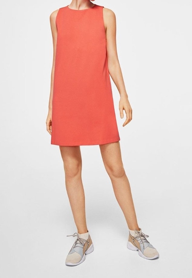Robe corail sans manches en ligne A portée avec des baskets athlétiques beiges et grises sur une personne debout sur un fond uni.
