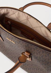 Καφέ τσάντα με σχέδιο και δερμάτινες λεπτομέρειες, χρυστό φερμουάρ και μπεζ εσωτερικό με φερμουάρ τσέπη και λεπτομέρειες με το λογότυπο.
