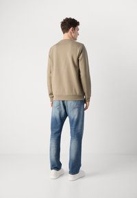 Beige sweatshirt with a crew neck, paired with light blue faded jeans and white sneakers. Smooth texture, casual fit, minimal design.