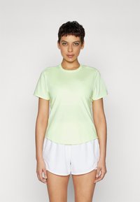 Camiseta atlética verde claro de manga corta y escote redondeado, combinada con pantalones cortos blancos. El tejido parece suave y ligero.