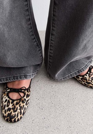Luipaardprint flats met een strikdetail, zwarte afwerking en een gladde synthetische textuur, gecombineerd met wijde zwarte denim broeken.