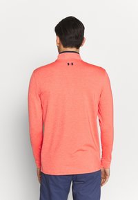 Pitkähihaista paitaa korallinvärissä, jossa on tummansininen reunus kauluksessa. Ominaisuuksina yksinkertainen muotoilu ja Under Armour -logo takana. Sileä pinta.