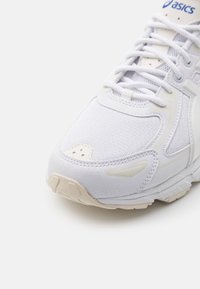 Vit sportig sneaker med överdel i mesh och syntetmaterial, texturerade detaljer, platta snörningar och en lätt sula med mönster för bra grepp.