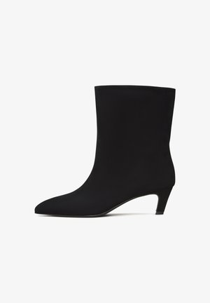 Schwarze Knöchelschuh mit glatter, eleganter Textur, spitzem Zehenbereich und niedrigem Kittenheel. Nahtloses Design ohne sichtbare Beschläge oder Muster.