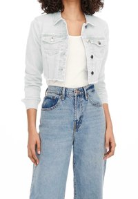 Ljusblå kort denimjacka med knäppning fram, två bröstfickor och rå fåll, kombinerad med högmidjade blåjeans.