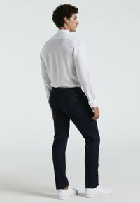 Witte linnen overhemd met lange mouwen en een klassieke kraag, gecombineerd met marineblauwe broeken en witte sneakers, die een casual pasvorm en subtiele textuur tonen.