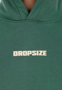 Un sweat à capuche vert avec le mot "DROPSIZE" imprimé en lettres majuscules blanches et en gras sur la poitrine.