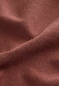 Tissu à texture douce avec des plis délicats dans une couleur brun chaud, montrant les détails fins du tissage.