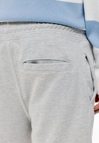 I pantaloni da tuta grigio chiaro presentano una tasca posteriore con apertura a fessura e una cintura elastica. La texture è morbida e liscia, adatta per un abbigliamento casual.