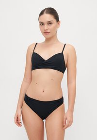 Black bikini set featuring a v-neck cropped top with adjustable straps and a ruched waistband on the bottom. Smooth texture, minimal design.