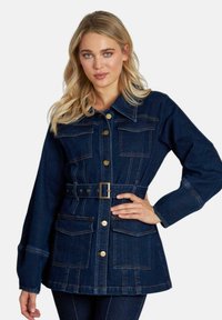 Chaqueta de mezclilla en azul oscuro con cierre de botones en el frente, cinturón en la cintura y cuatro bolsillos delanteros. Presenta un cuello puntiagudo y mangas largas con detalles de costura.