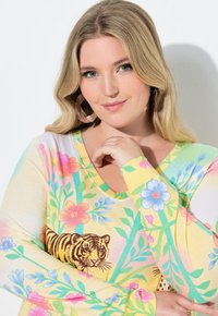 Długi rękaw z żółtą bazą, kolorowymi wzorami kwiatowymi oraz grafiką tygrysa, wykonany z miękkiego materiału, z dekoltem w serek.