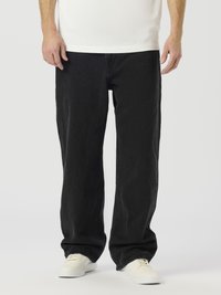 Crne traperice s opuštenim krojem, ravnim nogavicama i glatkom teksturom, uparene s bijelim tenisicama za kontrast.