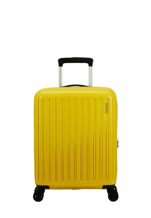 Valise jaune en plastique rigide avec un design à rainures verticales, poignée rétractable et quatre roues noires pour la mobilité. Fermeture éclair sur le côté.