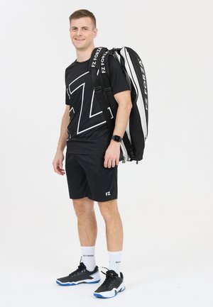 Svart atletiskt t-shirt med vitt logotyp, svarta shorts och svarta skor med blå accenter; bärande en svart och vit sportryggsäck.