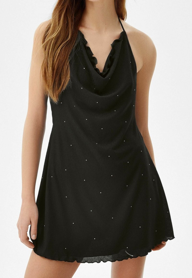 Černé halter šaty s texturovanou látkou, vodovým výstřihem a vroubkovaným lemem. Ozdobené drobnými bílými tečkami po celém povrchu.