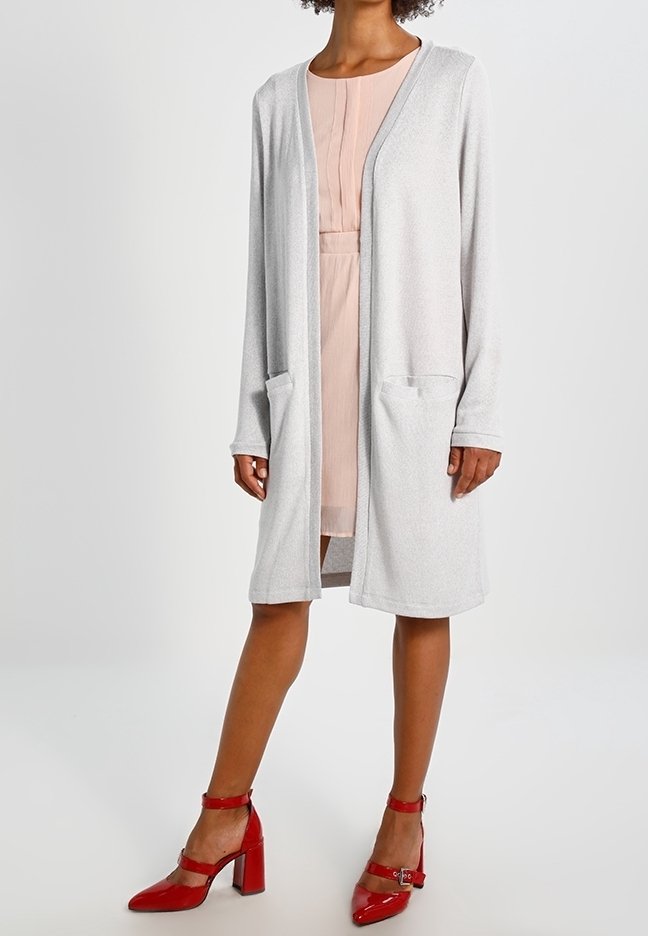 Dlouhý šedý kardigan s volnějším střihem, dvěma kapsami vpředu a otevřeným předním dílem, doplněný světle růžovými šaty a červenými lodičkami na vysokém podpatku.