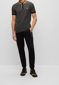 Polo shirt nero a motivo con accenti arancioni e neri, abbinato a jogger neri con logo discreto e sneaker nere con dettagli arancioni.